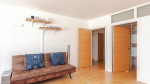 A modern living room with a brown leather sofa, two denim pillows, a white floor lamp, and a wooden shelf with electronic devices. - Cosy and Spacious 3 BD flat on Bermondsey St (London)