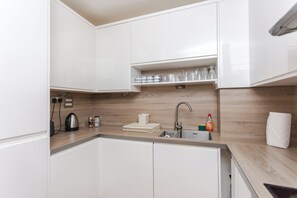 A modern kitchen with white cabinets, a wooden countertop, a sink, and various kitchen appliances. - Cosy and Spacious 3 BD flat on Bermondsey St (London)