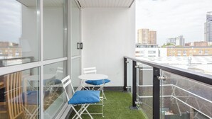Un balcon doté d’une balustrade en verre, une petite table, deux chaises et un coussin bleu.