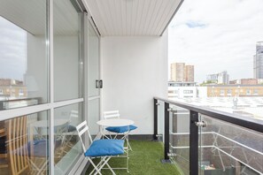 Un balcon doté d’une balustrade en verre, une petite table, deux chaises et un coussin bleu.