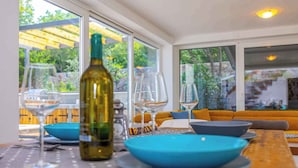 Un coin repas avec une table dressée pour deux personnes, une bouteille de vin et une vue sur l’extérieur grâce à de grandes fenêtres.