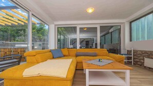 Un salon moderne avec un canapé d’angle jaune, une table basse en bois et une vue sur un jardin grâce à de grandes fenêtres.