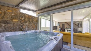 Un bain à remous situé dans un espace extérieur abrité, avec des murs en pierre et une vue sur un canapé jaune et un escalier à l’intérieur.