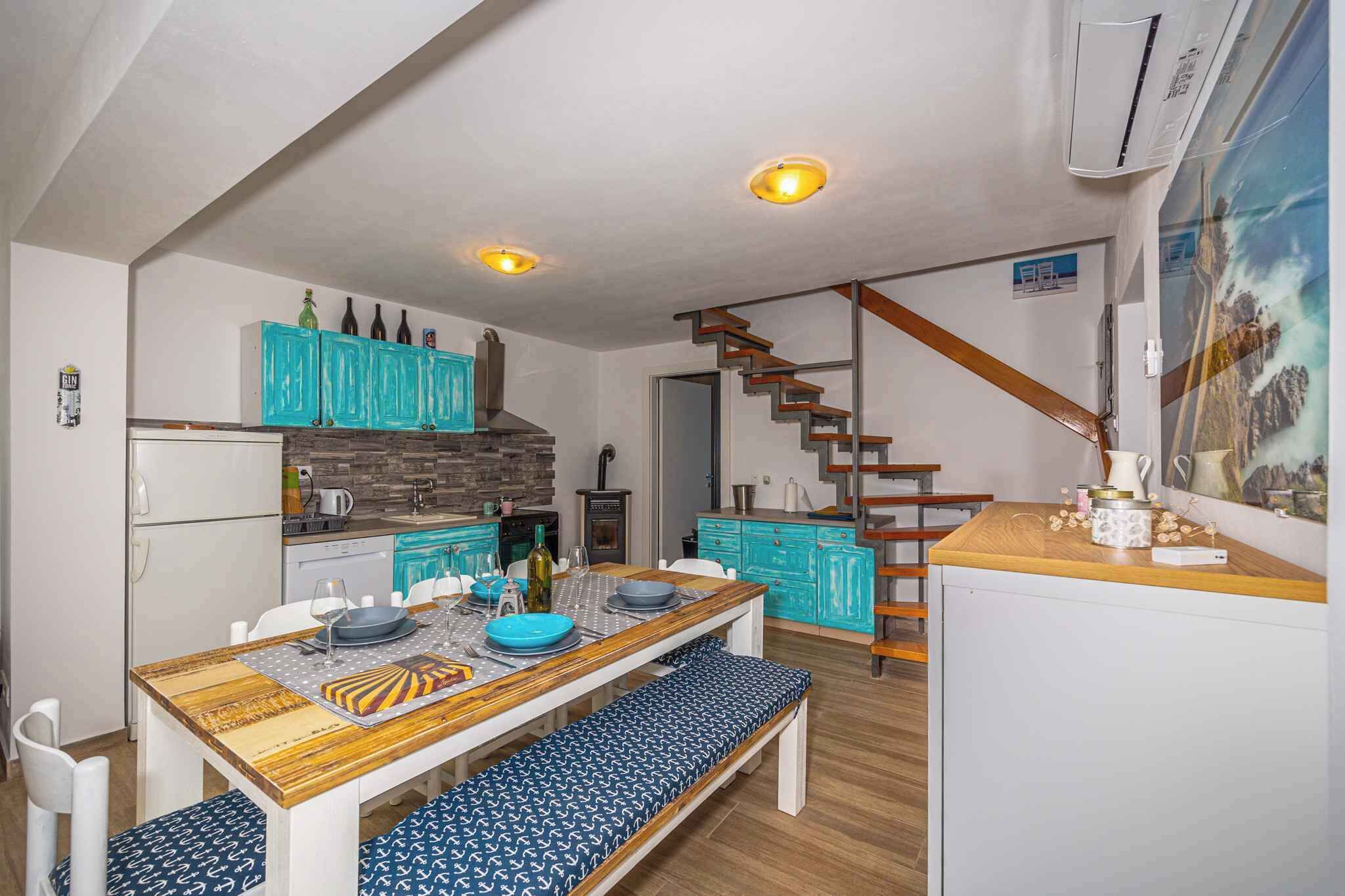 A compact kitchen with a wooden table, teal cabinets, and a staircase leading to another level.