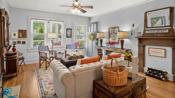 A cozy living room with a sofa, a wooden coffee table, and a fireplace. There are framed pictures on the wall and a window with blinds.