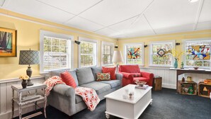 A living room with a grey sofa, red and orange cushions, a white coffee table, and a window with a stained glass view.