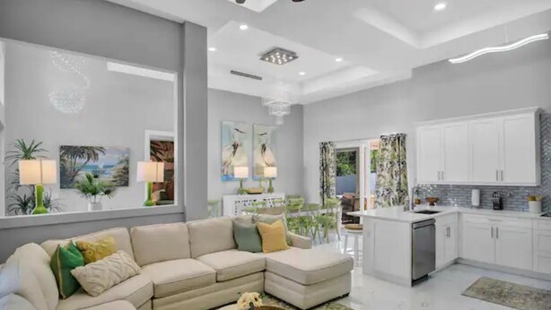 A modern living room with a beige sectional sofa, a dining area with a table and chairs, and a kitchen with white cabinets and a dishwasher. - Luxurious SW Florida Pool Home (Cape Coral)
