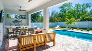 A poolside area with a wooden bench, a dining table, and chairs. - Luxurious SW Florida Pool Home (Cape Coral)