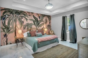 A bedroom with a bed, a nightstand, a lamp, a mirror, and a view of the outside.