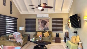 Una sala de estar con ventilador de techo, televisor de pantalla plana y sofá con cojines decorativos.