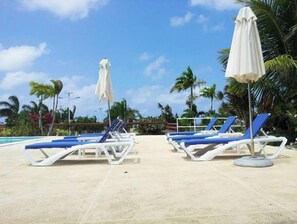A poolside area with lounge chairs and umbrellas, surrounded by palm trees and a clear sky. - Gigi's Chateau-Villa Getaway near OCHO RIOS, JA! (St. Ann Parish)