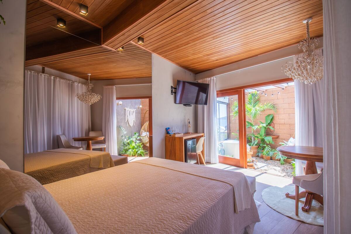 A hotel room with a bed, a desk, a television, and a balcony with plants.