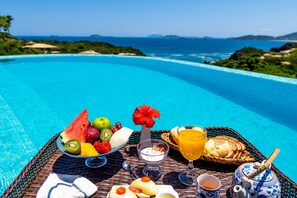 A breakfast setup by a pool with tropical fruits, bread, and beverages. - GRINGOS BOUTIQUE HOTEL (Búzios)
