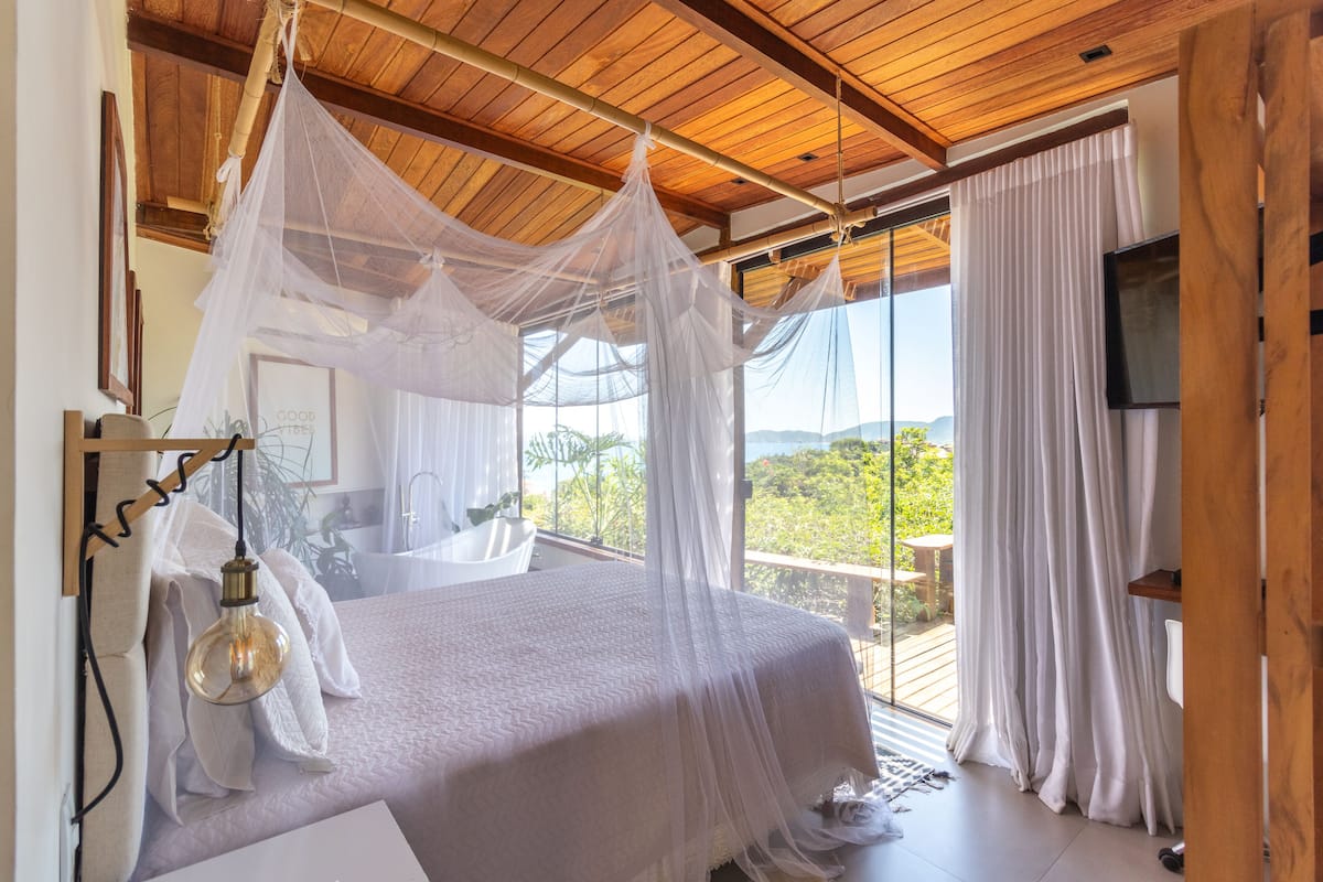 A bedroom with a canopy bed, a large window, and a TV.