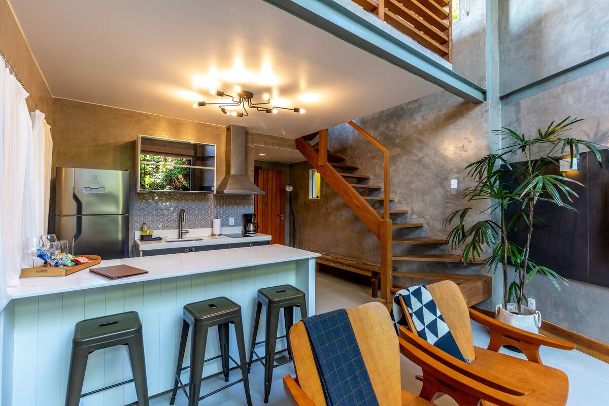 A modern kitchen with a central island, bar stools, and a staircase leading to an upper level.