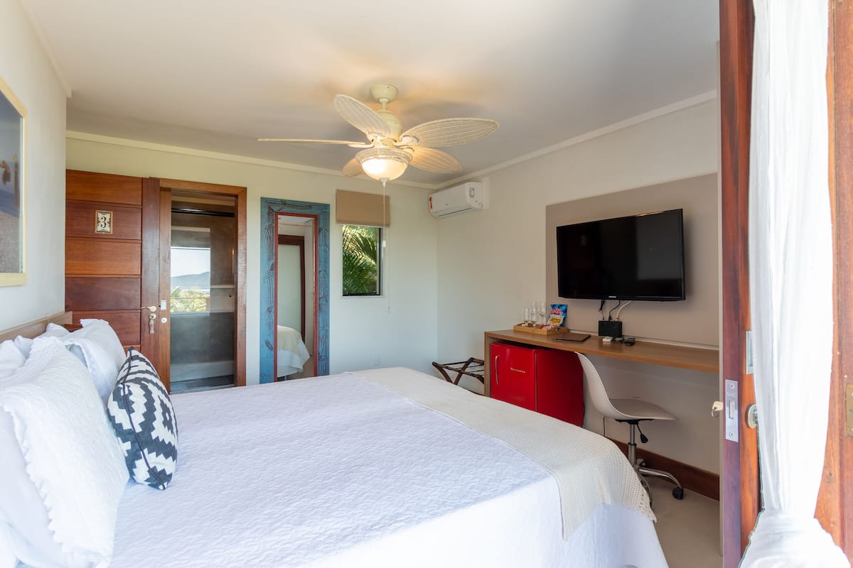 A hotel room with a bed, a desk with a computer, a TV, and a ceiling fan.