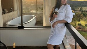 A person in a white robe on a balcony with a view of a sunset and a hot tub inside. - Euetu na Lapinha da Serra (Santana do Riacho)