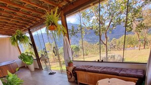 A cozy room with a wooden ceiling, large windows, a cushioned bench, and potted plants. - Euetu na Lapinha da Serra (Santana do Riacho)