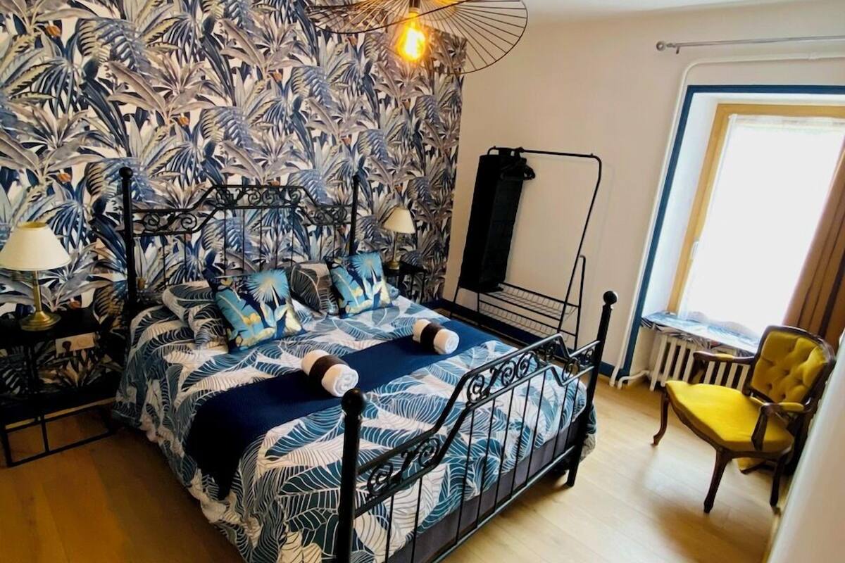 Une chambre à coucher avec un lit, une table de chevet, une lampe, une chaise et une fenêtre.