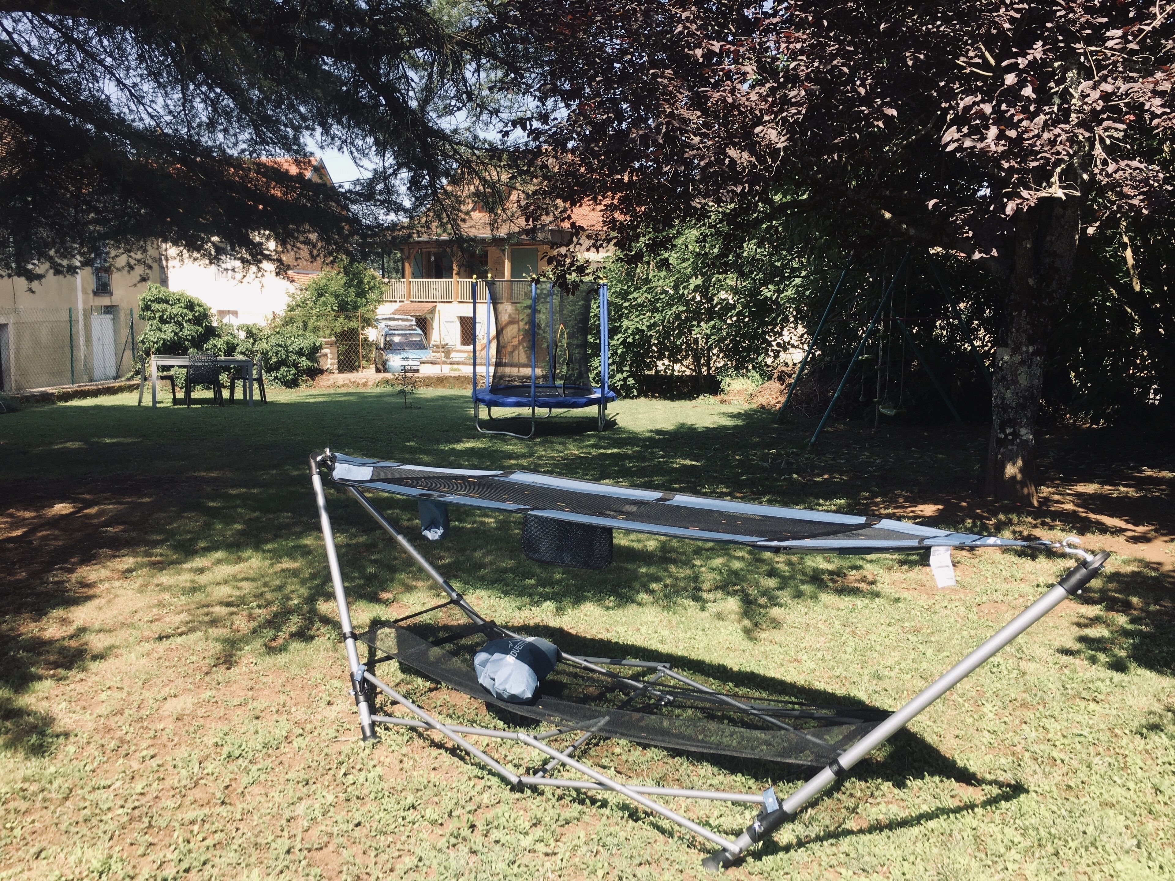 A trampoline in a backyard with a swing set and a table.