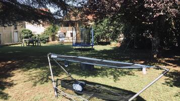 A trampoline in a backyard with a swing set and a table.