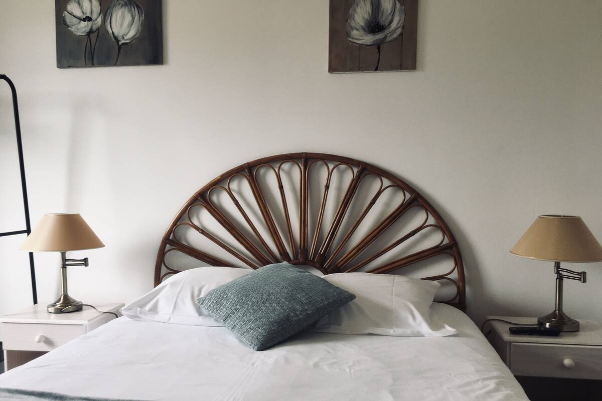 Un lit avec une tête de lit en bois, deux tables de chevet avec des lampes et deux tableaux accrochés au mur.