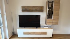 A modern living room with a flat-screen TV, a wooden cabinet with glass doors, and a white entertainment unit. - Cabinet Riedersteinblick in Rottach-Egern am Tegernsee  (Rottach-Egern)