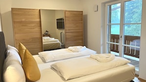 A bedroom with a bed, a wardrobe, a mirror, and a window with a view of trees. - Cabinet Riedersteinblick in Rottach-Egern am Tegernsee  (Rottach-Egern)