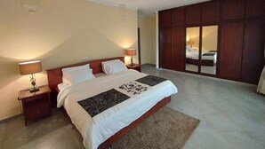 Een hotelkamer met een groot bed, twee nachtkastjes met lampen, een spiegel en uitzicht op een andere kamer door een schuifdeur.