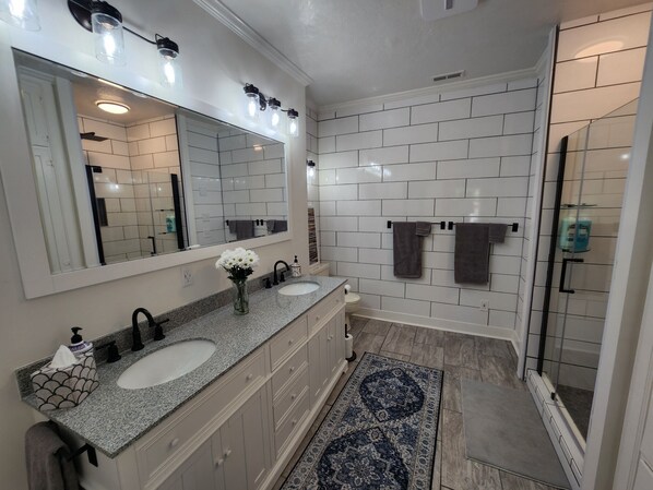 A modern bathroom with two sinks, a large mirror, and a walk-in shower.