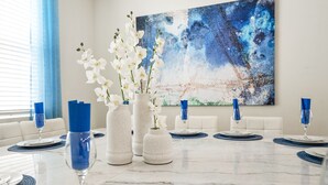 A dining table set with white plates, blue napkins, and white orchids in vases. - Solara 7BR with Private Pool/Game Room 22098 (Four Corners)