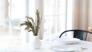 Et rundt spisebord med hvide tallerkener, bestik og en vase med tørrede blomster.