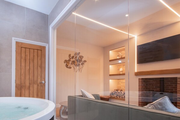A modern bathroom with a wooden door, a glass-enclosed shower area, a built-in seating area with cushions, and a fireplace.
