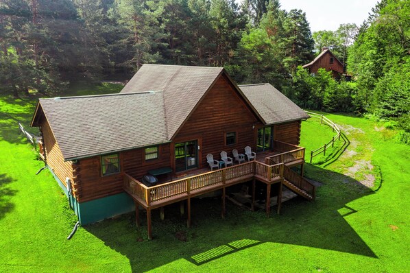 A wooden cabin with a deck, surrounded by lush greenery.