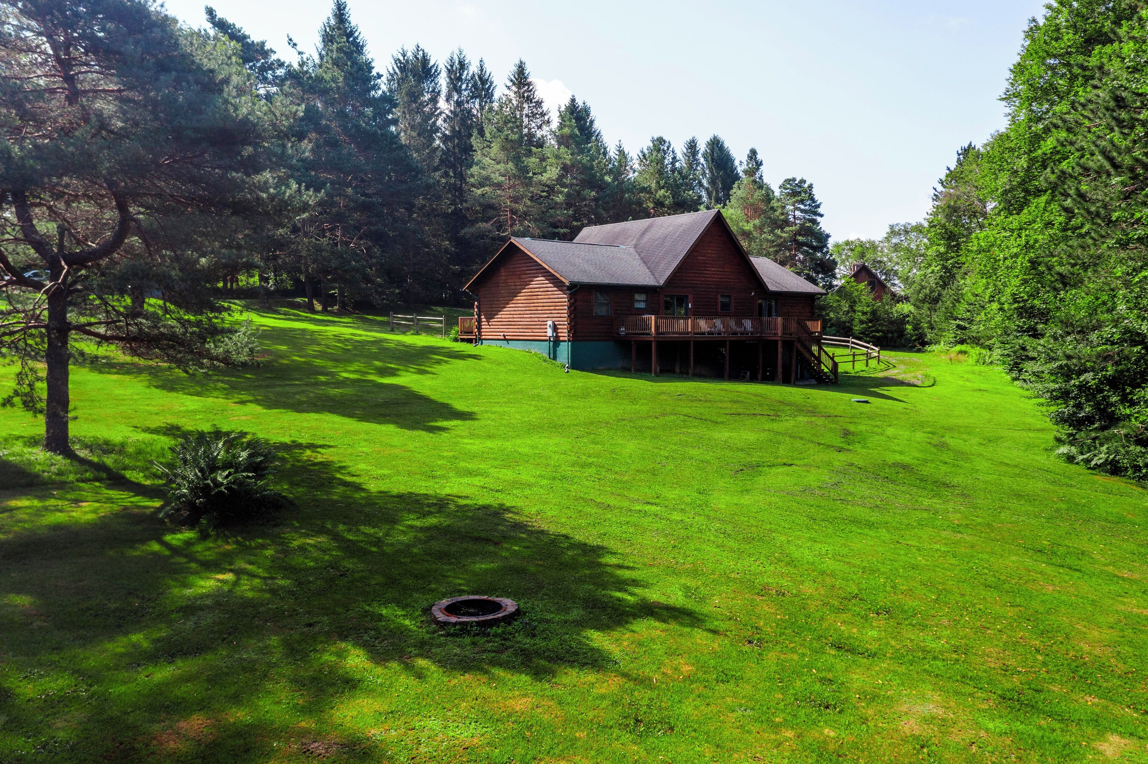 Eine Holzhütte mit einer Terrasse, umgeben von üppigem Grün und Bäumen.