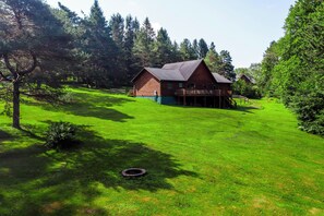 A wooden cabin with a deck, surrounded by lush green grass and trees.