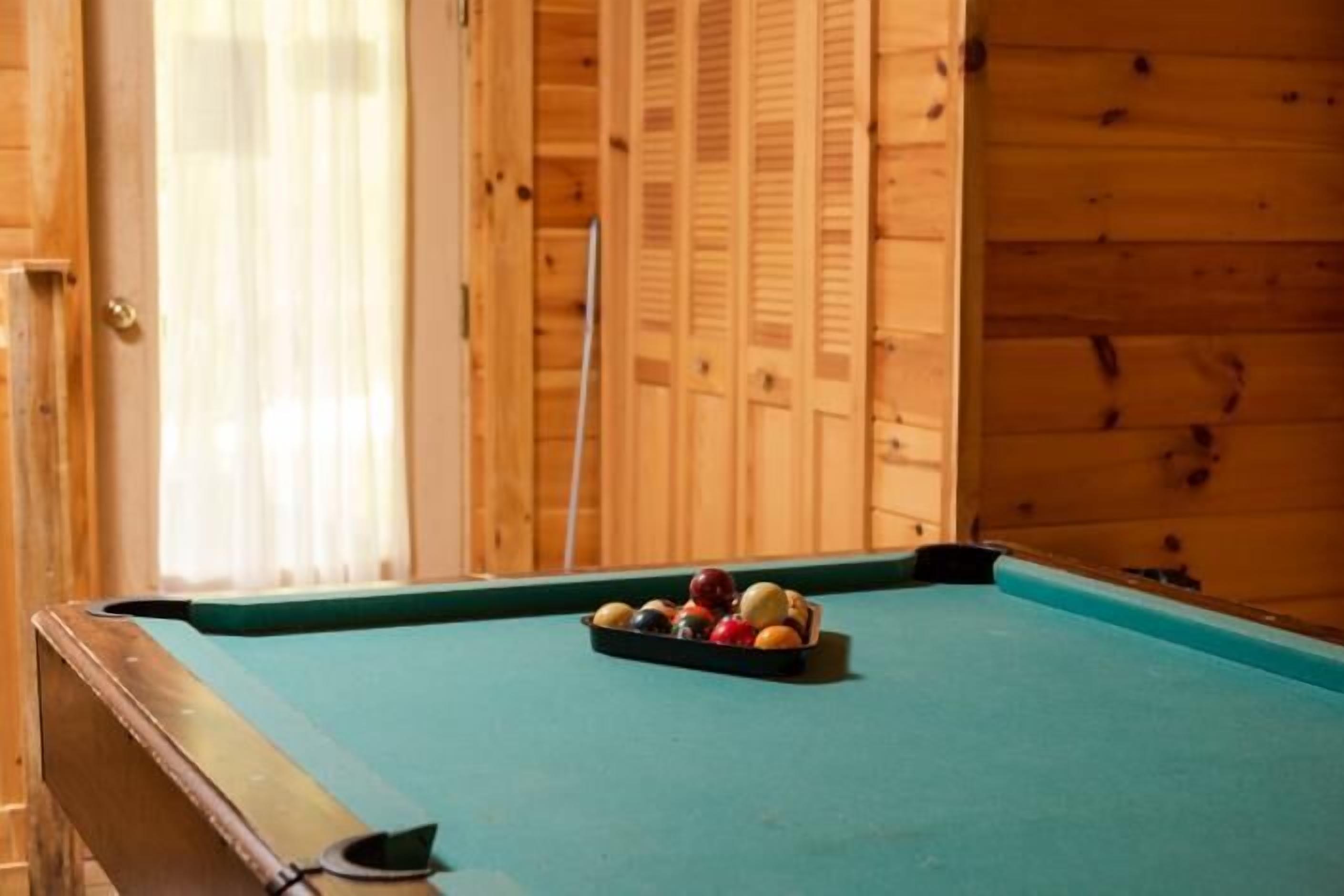 A pool table with balls in the center, a wooden wall, and a door with a curtain.