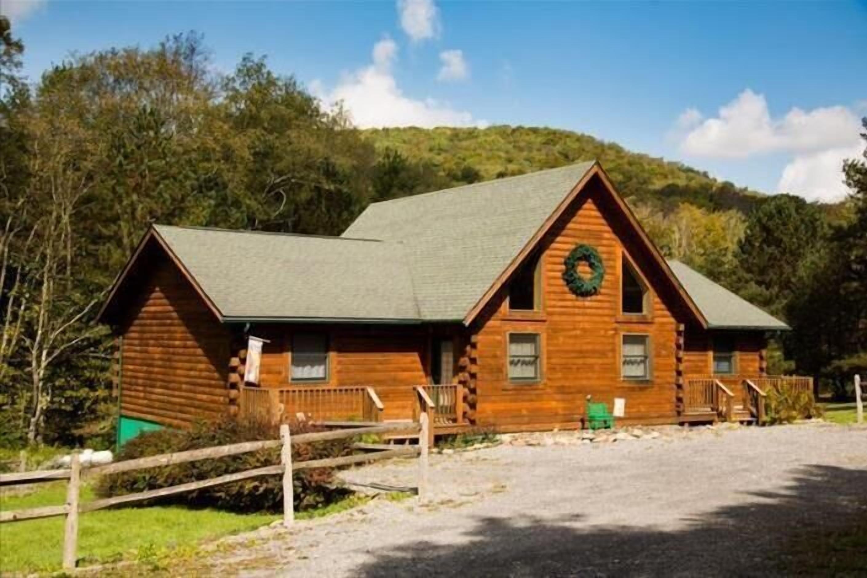 A log cabin with a green roof, a front porch, and a wreath on the door.