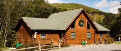 A log cabin with a green roof, a front porch, and a wreath on the door.