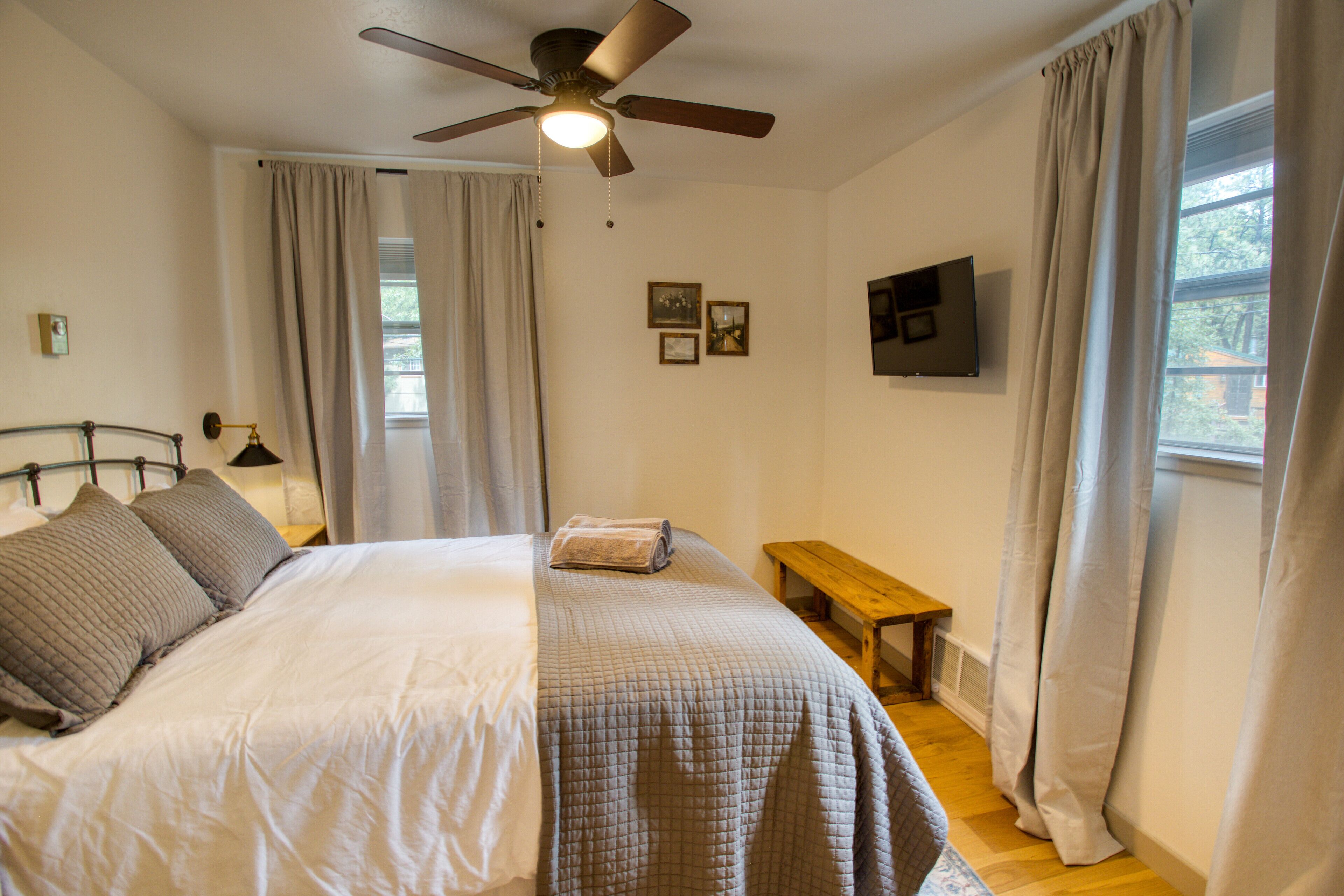 A bedroom with a bed, a ceiling fan, a TV, and a window with curtains.
