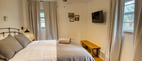 A bedroom with a bed, a ceiling fan, a TV, and a window with curtains.