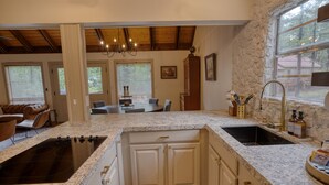 Uma cozinha com bancadas de granito, armários brancos, fogão embutido e uma janela grande.