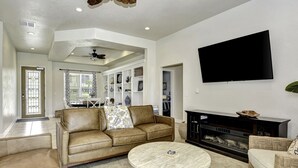 A living room with a brown leather sofa, a round coffee table, a fireplace, and a flat-screen TV mounted on the wall.