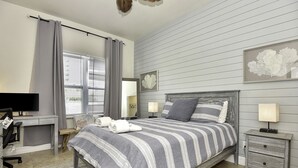 A bedroom with a bed, bedside tables, a desk, a chair, a TV, and a window with curtains.