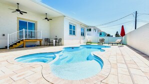 A backyard with a swimming pool, a covered patio area with chairs, and a staircase leading to a deck.