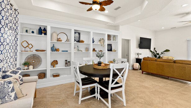 A spacious living room with a dining area, white furniture, and a ceiling fan.