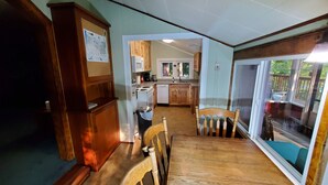 A dining area with a wooden table and chairs, a kitchen in the background, and a view through a glass door. - RiverPeace on the McKenzie (Blue River)