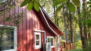A red wooden cabin with a window and an air conditioning unit, surrounded by a forest. - RiverPeace on the McKenzie (Blue River)