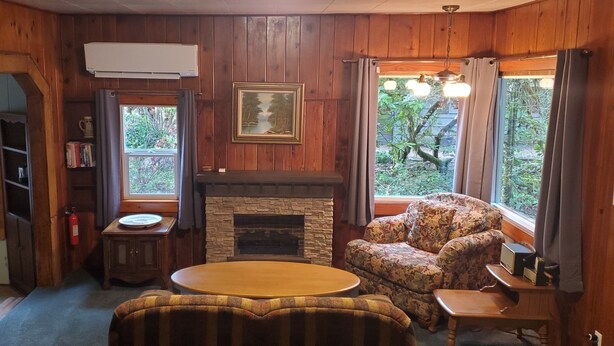 Een gezellige kamer met houten wanden, een stenen openhaard, een bloemenarmstoel, een ronde salontafel en een boekenplank.