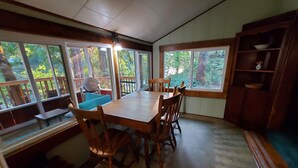 A dining area with a wooden table and chairs, large windows with a view of trees, and a wooden bench with a cushion. - RiverPeace on the McKenzie (Blue River)